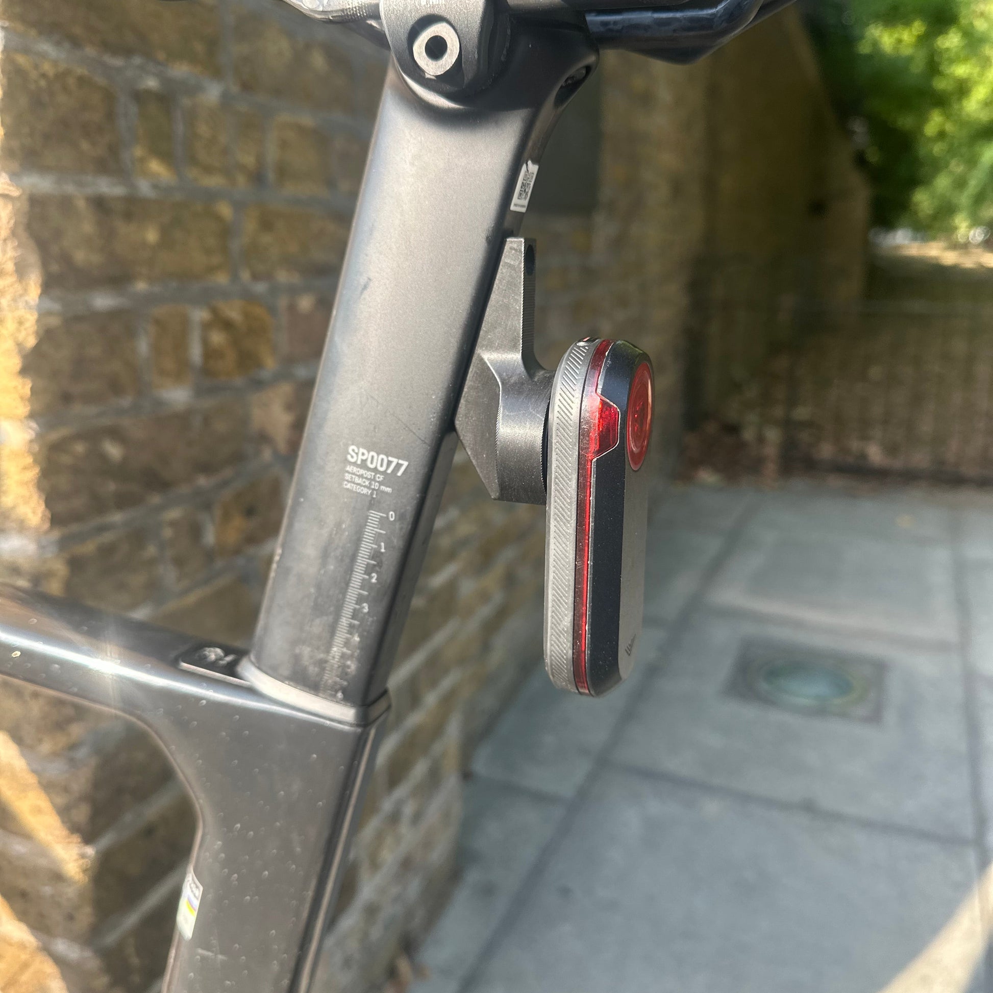 A close-up shot of a bicycle frame with a mounted rear light and a black saddle, set outdoors on a paved path.