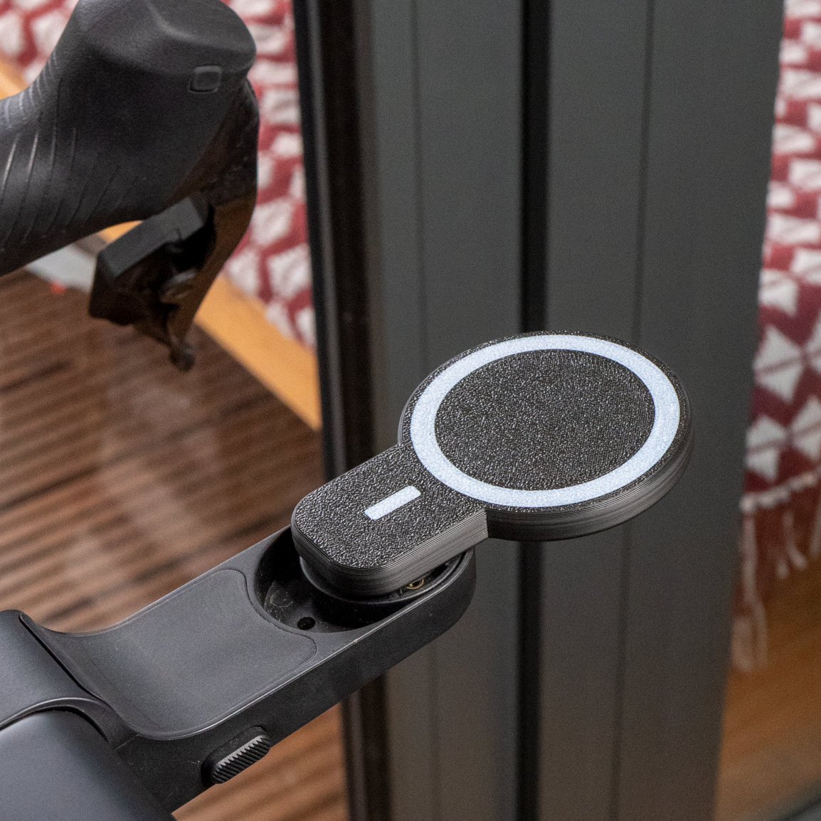 Close-up of a bicycle handlebar with a magnetic device attached, against a blurred indoor background.