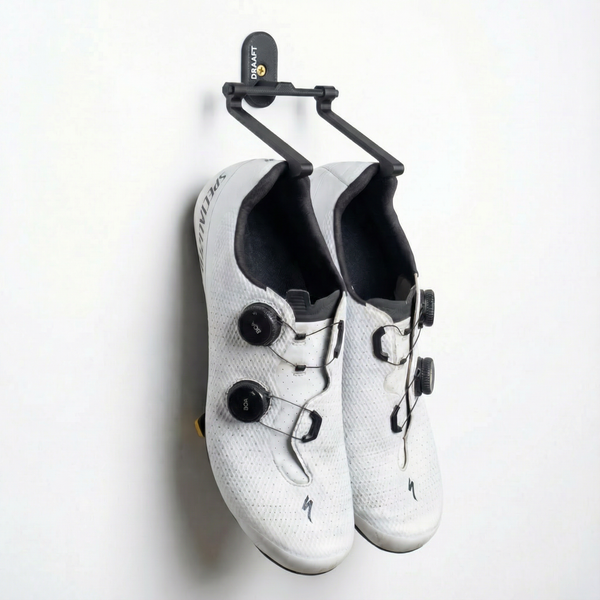 Pair of white cycling shoes hanging on a Draaft wall mounted shoe hanger